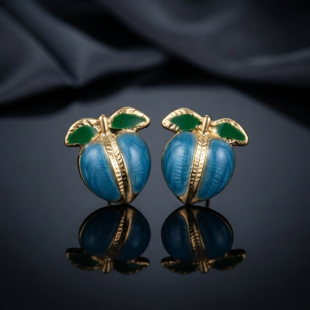 Gold-Tone Enamel Fruit Peach Stud Earrings in pink enamel worn on model ear with white satin backdrop showing round pink enamel peach stud with gold-tone ribbed seam and green enamel leaves close-up editorial portrait