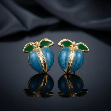 Gold-Tone Enamel Fruit Peach Stud Earrings in pink enamel worn on model ear with white satin backdrop showing round pink enamel peach stud with gold-tone ribbed seam and green enamel leaves close-up editorial portrait