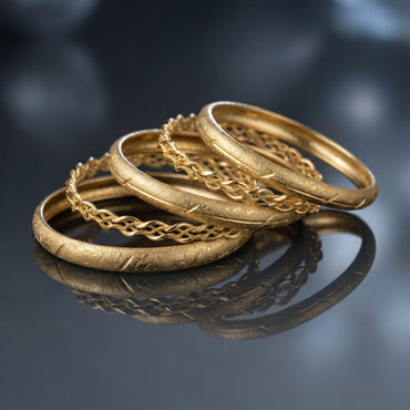 Four gold-tone bangles displayed together, with two engraved-texture and two braided chain-style designs.