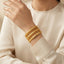 Wrist wearing four gold-tone bangles with engraved-texture and braided chain-style designs.