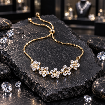 Gold-tone chain bracelet with five clear-petal flower motifs, star-shaped centres, a slider-style bead and two round-ended chain tails, displayed on dark slate.