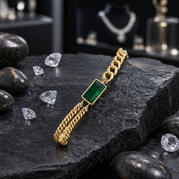 Gold-tone bracelet with a faceted green rectangular centre, slim border, chunky links on one side and two finer parallel chains on the other, displayed on dark slate.