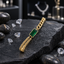 Gold-tone bracelet with a faceted green rectangular centre, slim border, chunky links on one side and two finer parallel chains on the other, displayed on dark slate.