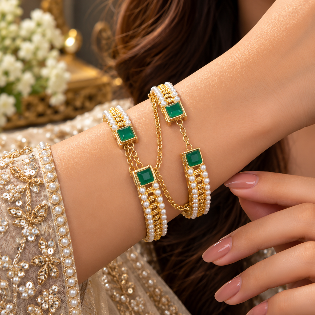 Model wearing two gold-tone bangles with green square accents, white pearl-look borders, textured gold-tone centres and draped chain details.