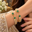 Model wearing two gold-tone bangles with green square accents, white pearl-look borders, textured gold-tone centres and draped chain details.