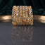 Gold-Tone Marquise and Round CZ Floral Leaf Open-Work Wide Bangle Set of 4 standing upright on dark grey mirror tray with emerald green velvet backdrop showing four matching wide gold bangles with open-work filigree leaf vine lattice marquise CZ settings round CZ pave and large oval champagne pink CZ solitaire accents with mirror reflection below