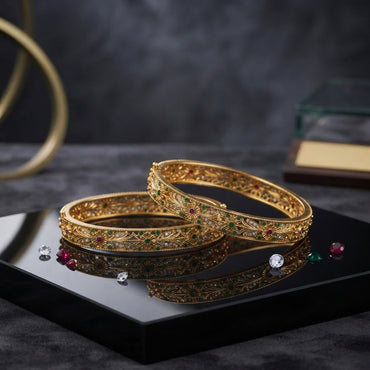 Gold-Tone Multi-Color CZ Daisy Floral Filigree Open-Work Wide Bangle Pair stacked on black mirror tray with dark marble backdrop and scattered ruby emerald and diamond CZ stones showing two matching wide gold bangles with dense floral filigree open-work gold lattice leaf and vine motifs and daisy flower accents with ruby-red and emerald-green CZ centers and white CZ petals with mirror reflection below