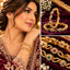 Gold-Tone Multi-Color CZ Floral Infinity Twist Slim Bangle Pair worn on model wrist in maroon embroidered bridal outfit with collage showing close-up on burgundy velvet tray and macro detail of ruby-red and emerald-green CZ floral rosettes on gold infinity twist bangle