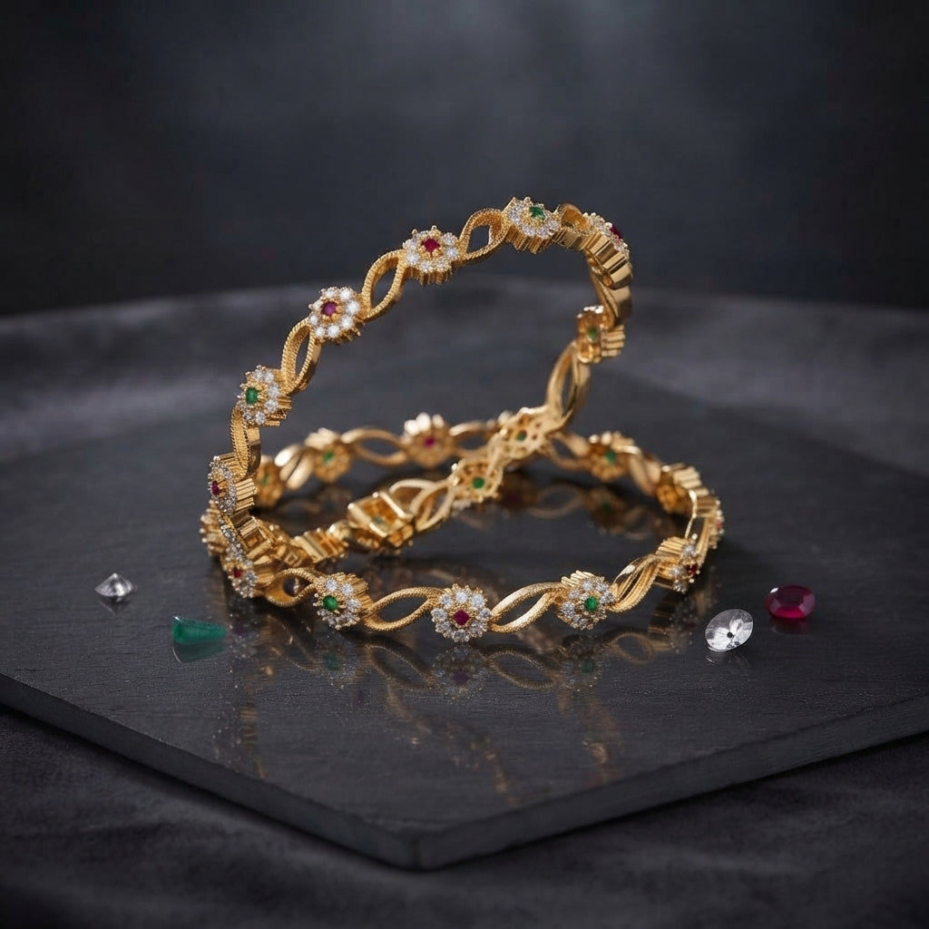 Gold-Tone Multi-Color CZ Floral Infinity Twist Slim Bangle Pair on dark slate stone surface with scattered ruby emerald and diamond CZ stones showing two matching slim gold bangles with continuous infinity twist gold links alternating with ruby-red and emerald-green CZ floral cluster rosettes with white CZ petals with mirror reflection below
