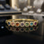Gold-tone bangle with multicolor halo-accent motifs, shown on a wrist.
