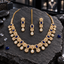 Gold-tone AD-style necklace with navy blue oval halo accents, pointed-petal flowers and clear-looking teardrop fringe, with matching earrings and bindia.