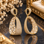 Gold-tone open teardrop drop earrings with oval tops, closely arranged small clear accents and larger rectangular and angular clear details.