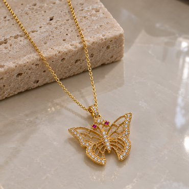 Gold-tone butterfly pendant necklace with openwork wings, clear-accent borders and body, pink antenna-tip details and a fine linked chain.