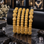 Five gold-tone textured bangles on a black display roll, with three rounded-segment inner bangles and two ornate outer bangles featuring larger decorative motifs.