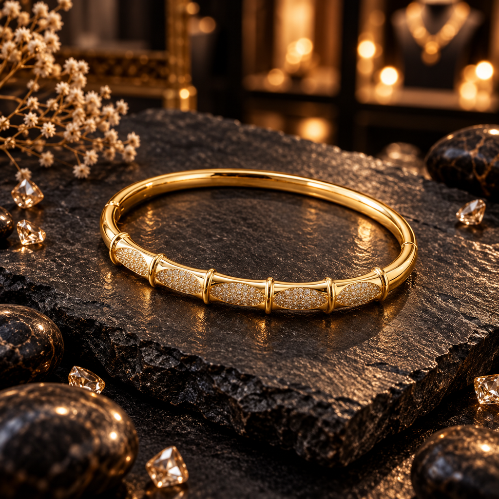 Gold-tone bangle with oval panels of small clear accents, raised gold-tone divider ridges and a smooth rear band.