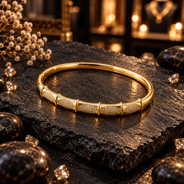 Gold-tone bangle with oval panels of small clear accents, raised gold-tone divider ridges and a smooth rear band.