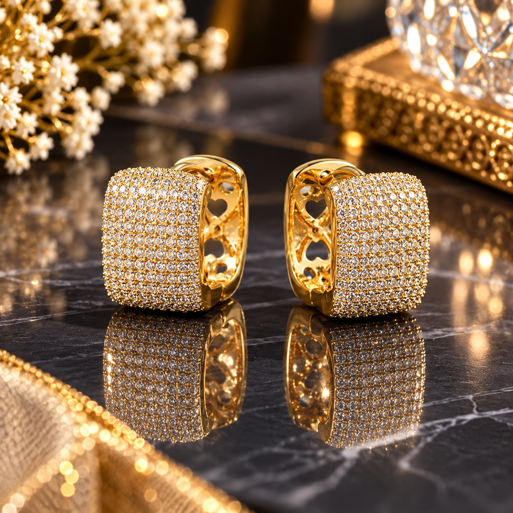 Pair of gold-tone rounded rectangular huggie hoop earrings with clear pavé-style accents and interior heart-shaped cutouts.