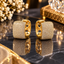Pair of gold-tone rounded rectangular huggie hoop earrings with clear pavé-style accents and interior heart-shaped cutouts.