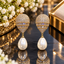 Gold-tone earrings with embellished tapered tops, two rectangular clear-accent bands and ivory-white teardrop pearl-look drops.