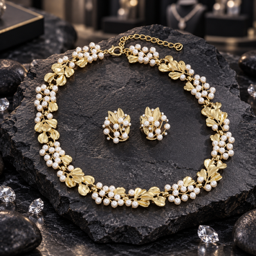 Gold-tone floral leaf necklace with white pearl-look clusters, lobster-style clasp and extension chain, displayed with matching earrings on dark slate.