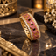 Gold-tone ornate band ring with small pink round accents, dark-red rectangular accents, clear-accent borders and openwork sides.