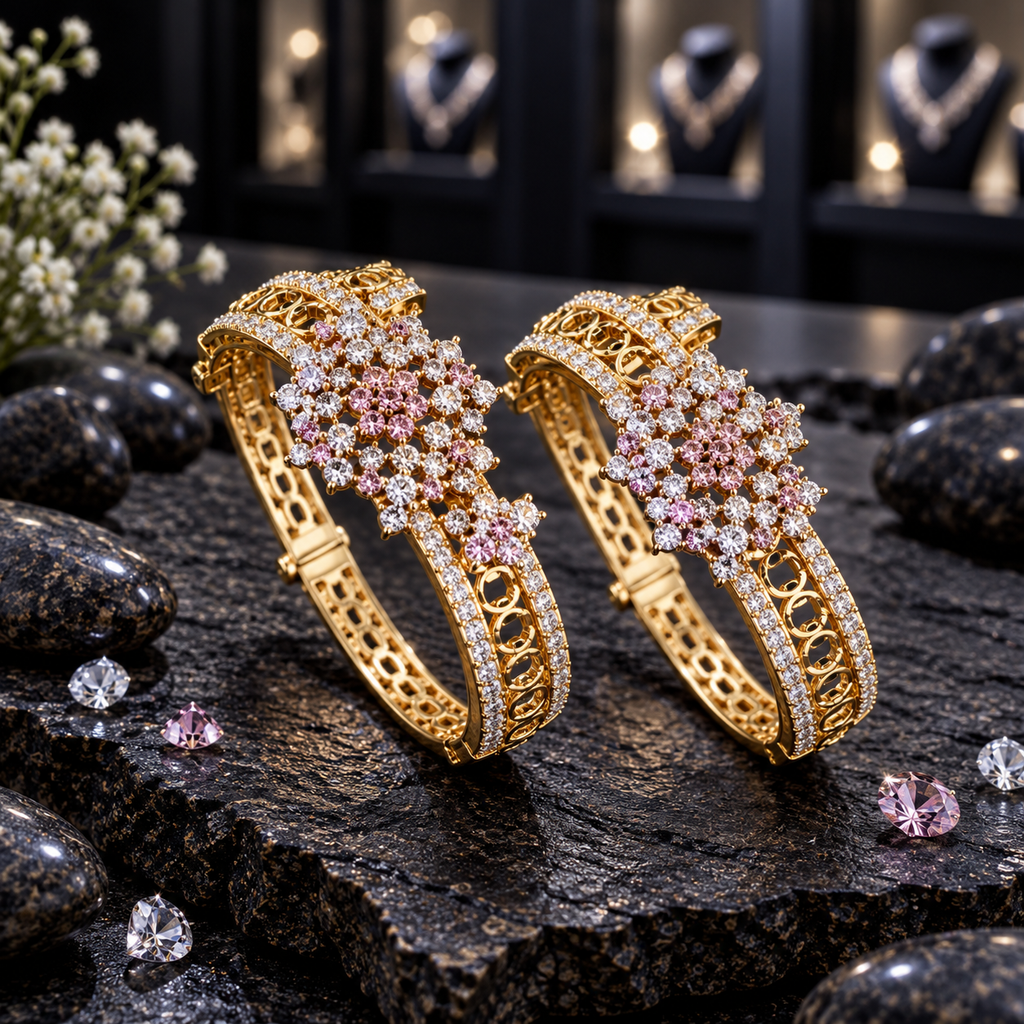 Pair of gold-tone openwork bangles with pink and clear floral clusters and clear accent borders, displayed upright on dark stone.