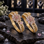 Pair of gold-tone openwork bangles with pink and clear floral clusters and clear accent borders, displayed upright on dark stone.