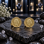 Pair of round gold-tone coin earrings with raised side-profile portraits, decorative lettering and detailed borders, displayed on dark stone.