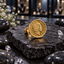Gold-tone ring with a round coin-style face featuring a crowned portrait, decorative lettering and dotted border on a dark stone display.