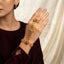 Gold-tone Indian Rajwari floral hathphool hand harness with red and green accents, shown worn on a hand.