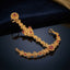 Gold-tone floral hathphool hand harness with red-toned accents, shown on a dark surface.
