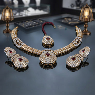 Gold-tone necklace with clear faceted accents and red details, matching earrings, and a coordinating maang tikka.