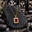 Gold-tone linked-chain necklace with a deep ruby-coloured rectangular centre, rounded segmented clear-accent halo and accented bail.