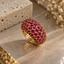Gold-tone domed cluster ring with round pink-red faceted accents and bead-like setting details.