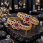 Pair of gold-tone openwork bangles with red floral clusters and clear accent borders, displayed on dark slate.