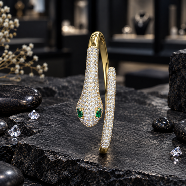 Gold-tone cuff-style bracelet displayed upright, with a single clear accent-covered snake head, two green eye details, a narrow rounded opposite end and a smooth gold-tone back band.