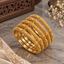 Gold-tone bangles arranged on marble, showing dotted textured sections, ribbed rounded details, and decorative scroll patterns.