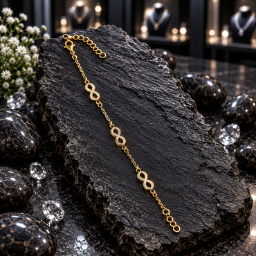Gold-tone fine chain bracelet with three open infinity-shaped motifs, small connecting rings, larger round end links and a lobster-style clasp, displayed lengthwise on dark slate.