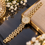 Gold-tone zircon watch-style bracelet with a round clear-accent centre, visible hand-like details and staggered rectangular links.