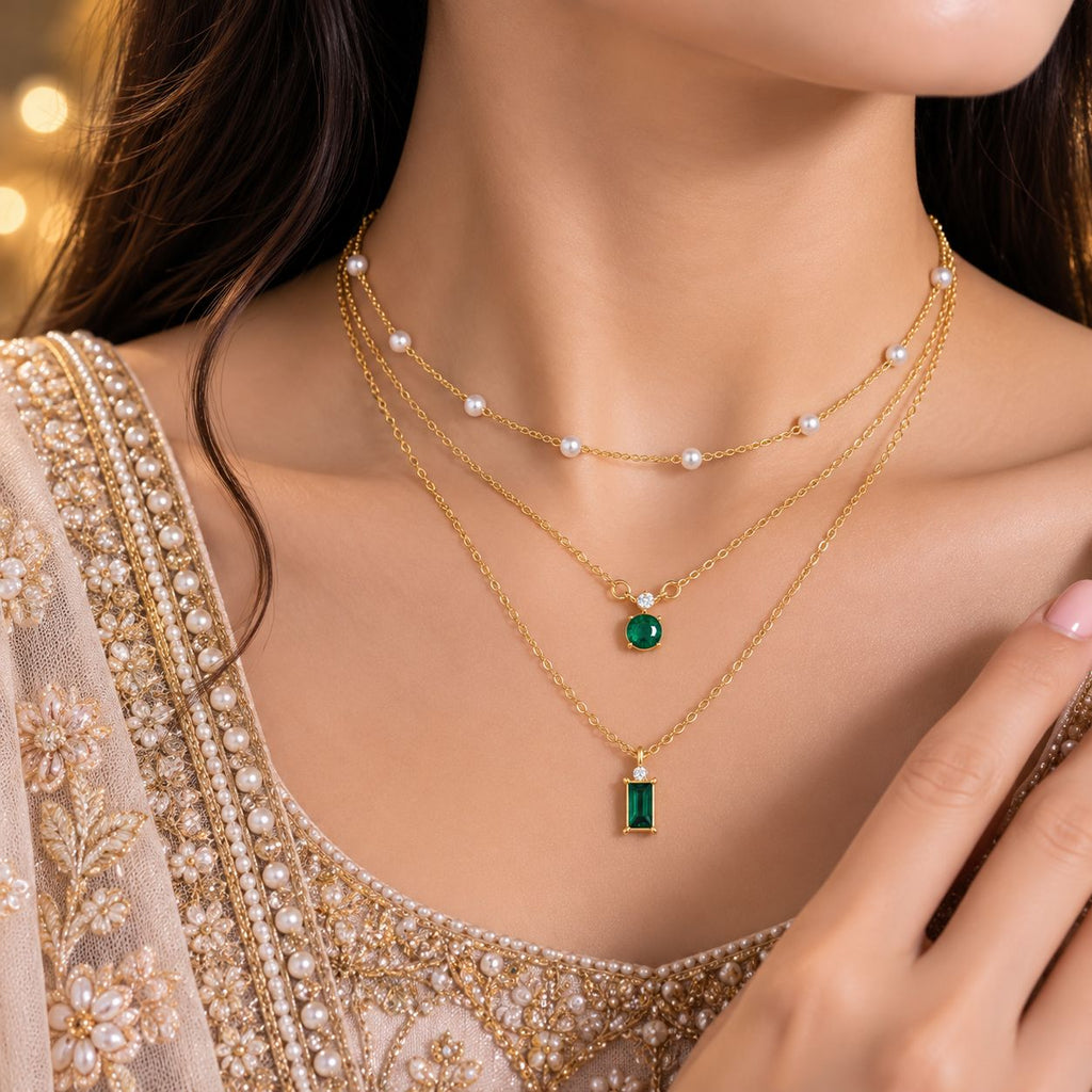 Gold Triple-Layer Pearl Station & Emerald CZ Dual Pendant Layered Necklace Set worn by bridal model in pearl-embroidered lehenga with gold bokeh backdrop