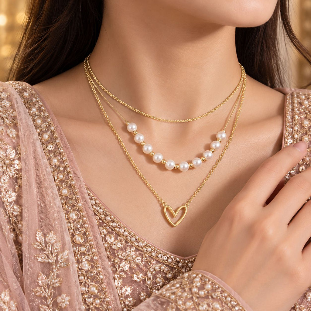 Gold Triple-Layer Pearl Station & Open Heart Pendant Layered Necklace worn by bridal model in pink embroidered lehenga with gold bokeh backdrop
