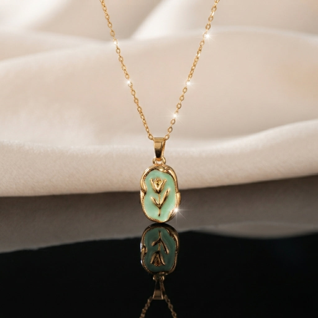 Gold Tulip Enamel Oval Pendant Necklace in mint green enamel flat lay on black mirror surface with white silk backdrop showing raised 3D gold tulip motif on mint green oval pendant with gold cable chain and sparkle effect with mirror reflection below