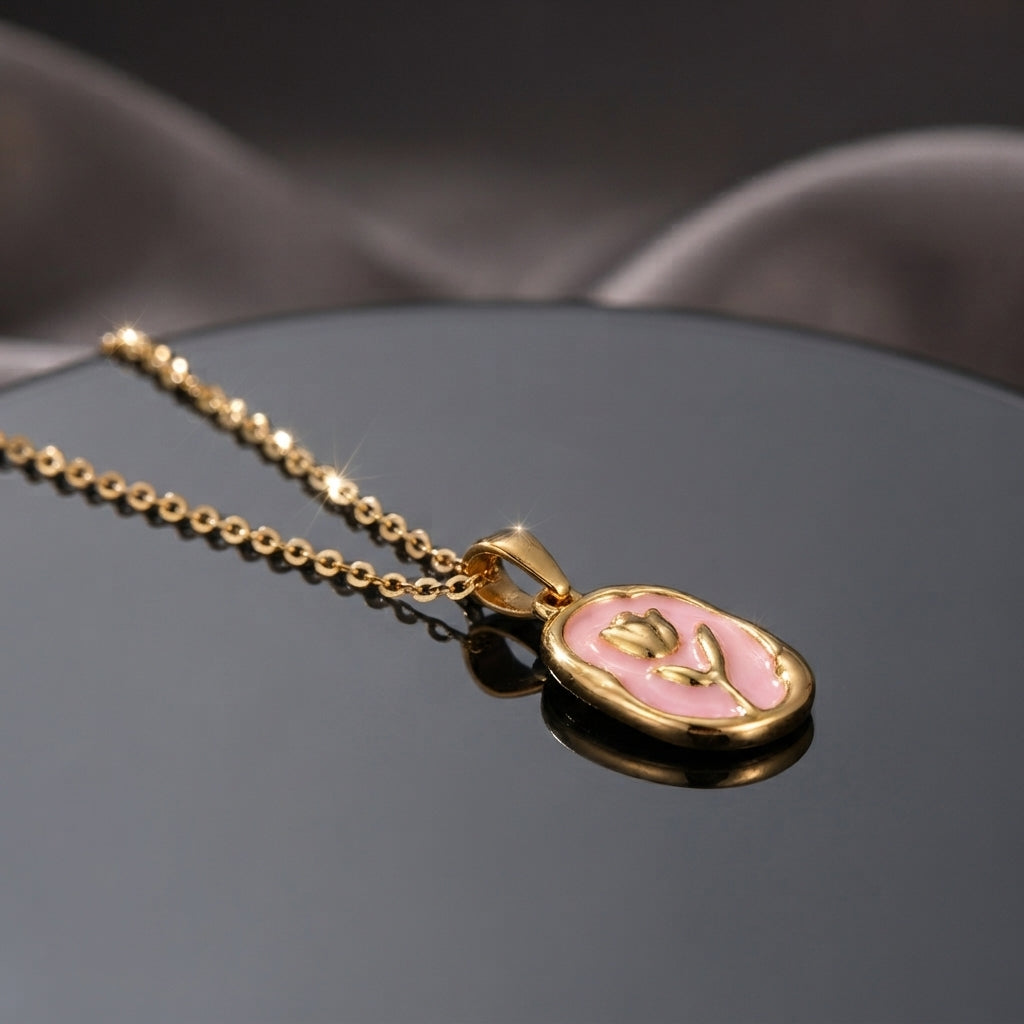 Gold Tulip Enamel Oval Pendant Necklace in blue grey enamel flat lay on black mirror surface with dark and beige fabric backdrop showing raised 3D gold tulip motif with CZ accents on blue grey oval pendant with gold cable chain and sparkle effect with mirror reflection below
