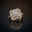 22K Gold-Tone White CZ Open Petal Rose Cluster & Pavé Twisted Rope Shoulder Cocktail Ring on dark grey mirror surface with warm gold bokeh light backdrop