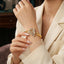 Gold White CZ and Ruby Red Butterfly Pave Hinged Cuff Bangle lifestyle editorial shot worn on model wrist with cream ivory blazer in warm luxury boutique setting showing 22K warm yellow gold-tone hinged cuff bangle with large 3D sculptural butterfly featuring dense micro-pave white CZ wings with engraved vein detailing vivid ruby red CZ body and pave CZ flower-tipped antennae
