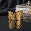 Gold Wide Botanical Leaf Cutwork Open Cuff Bangle in 18K gold-tone PVD brushed satin stainless steel on dark grey mirror surface with black silk backdrop and white dried flowers showing extra wide open cuff with flowing overlapping botanical leaf cutwork top edge and fine engraved leaf vein details with mirror reflection below