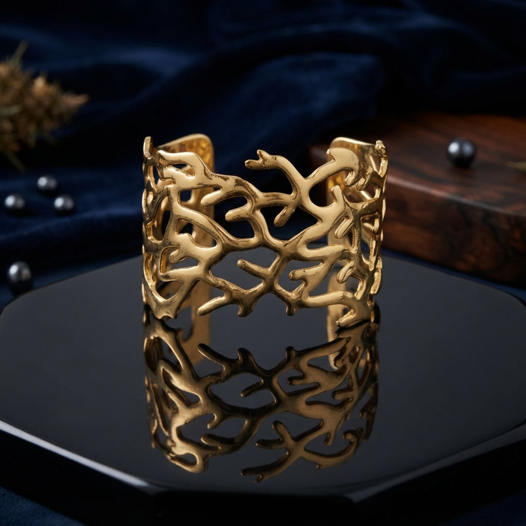 Gold Wide Coral Branch Cutwork Open Cuff Bangle in 18K antique gold-tone PVD matte satin stainless steel on dark navy hexagonal ceramic tile with dark navy silk backdrop dark pearls and dried botanicals showing extra wide open cuff with dense organic coral branch reef cutwork lattice irregular branching arms and organic top edge silhouette with mirror reflection below