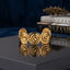Gold Wide Spiral Disc Open Cuff Bangle in 18K antique gold-tone PVD matte satin stainless steel on dark navy hexagonal mirror surface with Vogue and Bazaar books and dried botanicals backdrop showing wide open cuff with row of 5-6 large raised 3D Archimedean spiral disc motifs and scalloped top and bottom edges with mirror reflection below