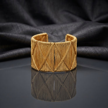 Gold Wire-Wrapped Crosshatch Wide Cuff Bangle standing upright on dark grey mirror surface with black silk backdrop showing fully wire-wrapped wide open-back cuff with diamond X crosshatch pattern overlay in brushed gold-tone finish with mirror reflection below