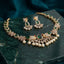 South Indian-style gold-tone floral necklace and matching drop earrings with red accents and pearl-look drops, displayed on a dark surface.